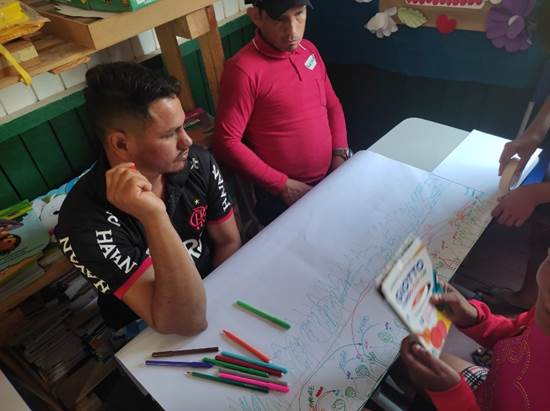 Pessoas sentadas ao redor de uma mesa com um livro na mão
Descrição gerada automaticamente com confiança média